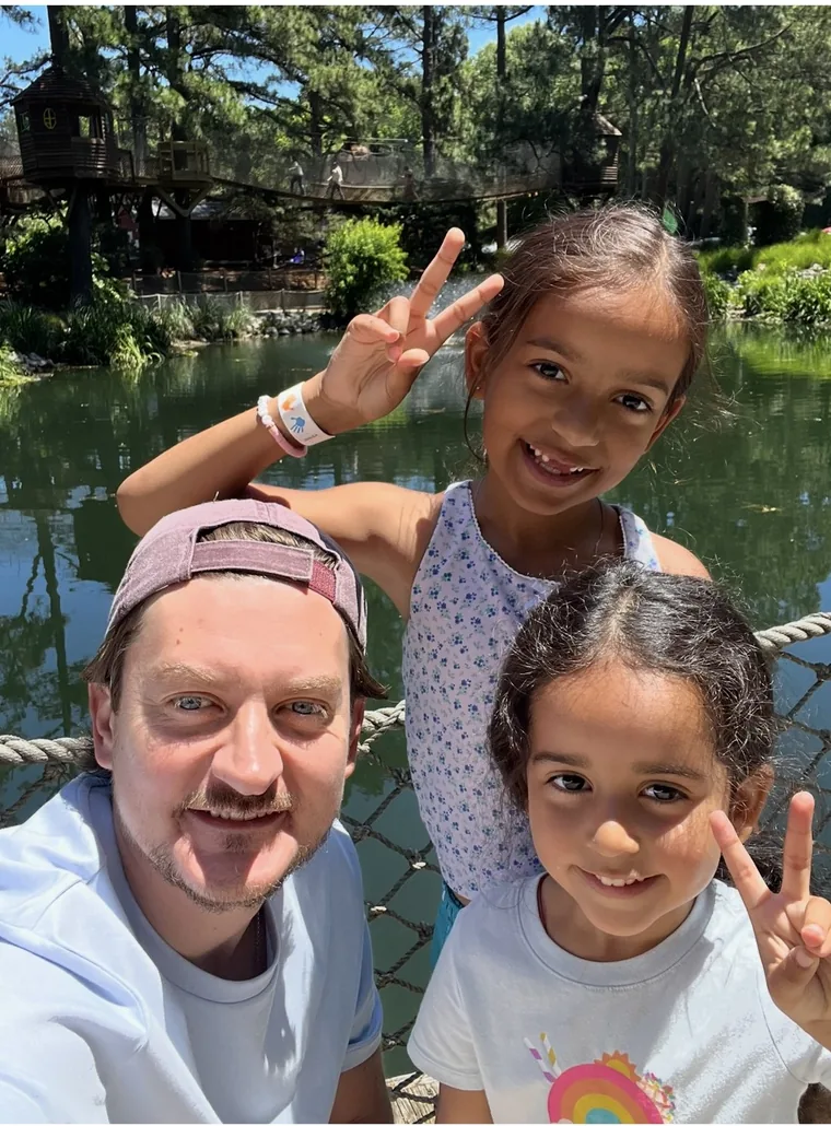 Konstantin with his two daughters, smiling on a rope bridge by a pond